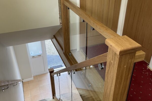 Staircase and landing renovation in Rugby featuring bespoke clad posts, increased handrail height, and toughened glass balustrade panels set into grooves. A modern and safer staircase transformation by Robert McVey Staircases.
