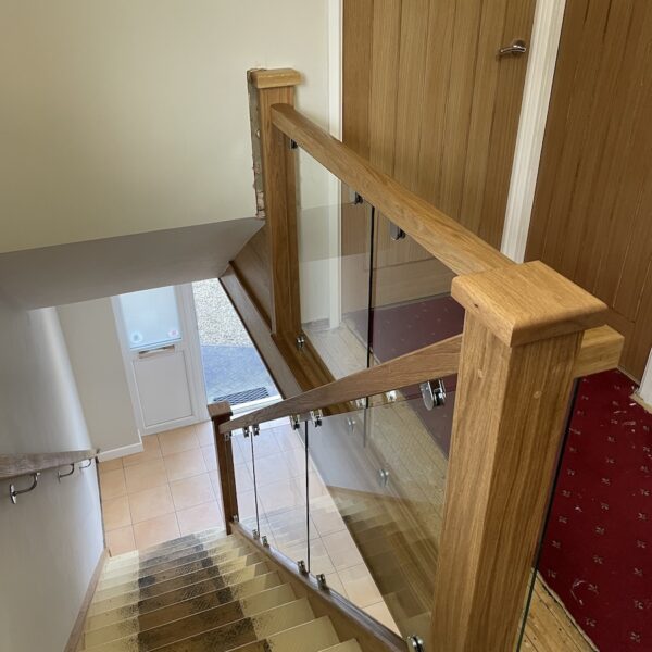 Staircase and landing renovation in Rugby featuring bespoke clad posts, increased handrail height, and toughened glass balustrade panels set into grooves. A modern and safer staircase transformation by Robert McVey Staircases.