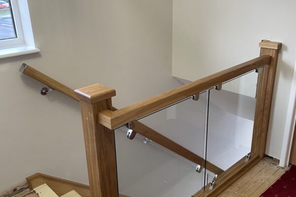 Staircase and landing renovation in Rugby featuring bespoke clad posts, increased handrail height, and toughened glass balustrade panels set into grooves. A modern and safer staircase transformation by Robert McVey Staircases.