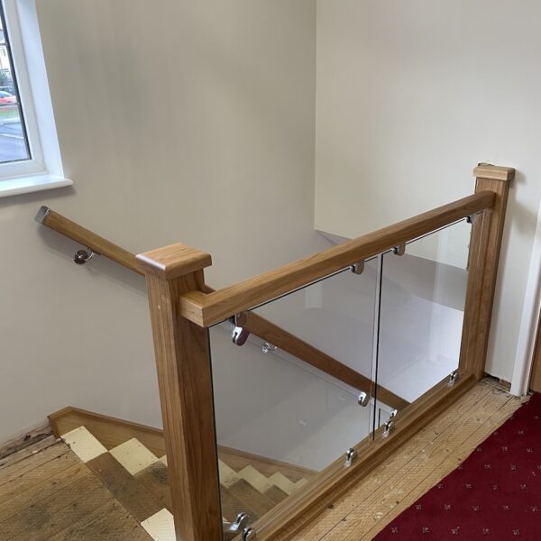 Staircase and landing renovation in Rugby featuring bespoke clad posts, increased handrail height, and toughened glass balustrade panels set into grooves. A modern and safer staircase transformation by Robert McVey Staircases.