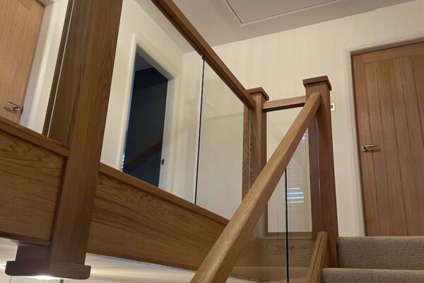 Staircase renovation in Broughton Astley featuring American white oak components with a clear oil finish and glass balustrade panels mounted on chrome brackets. A bright, modern hallway transformation completed in two days by Robert McVey Staircases.