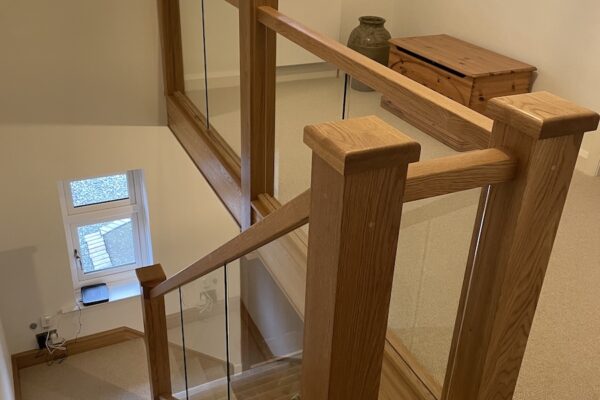 Staircase renovation in Broughton Astley featuring American white oak components with a clear oil finish and glass balustrade panels mounted on chrome brackets. A bright, modern hallway transformation completed in two days by Robert McVey Staircases.