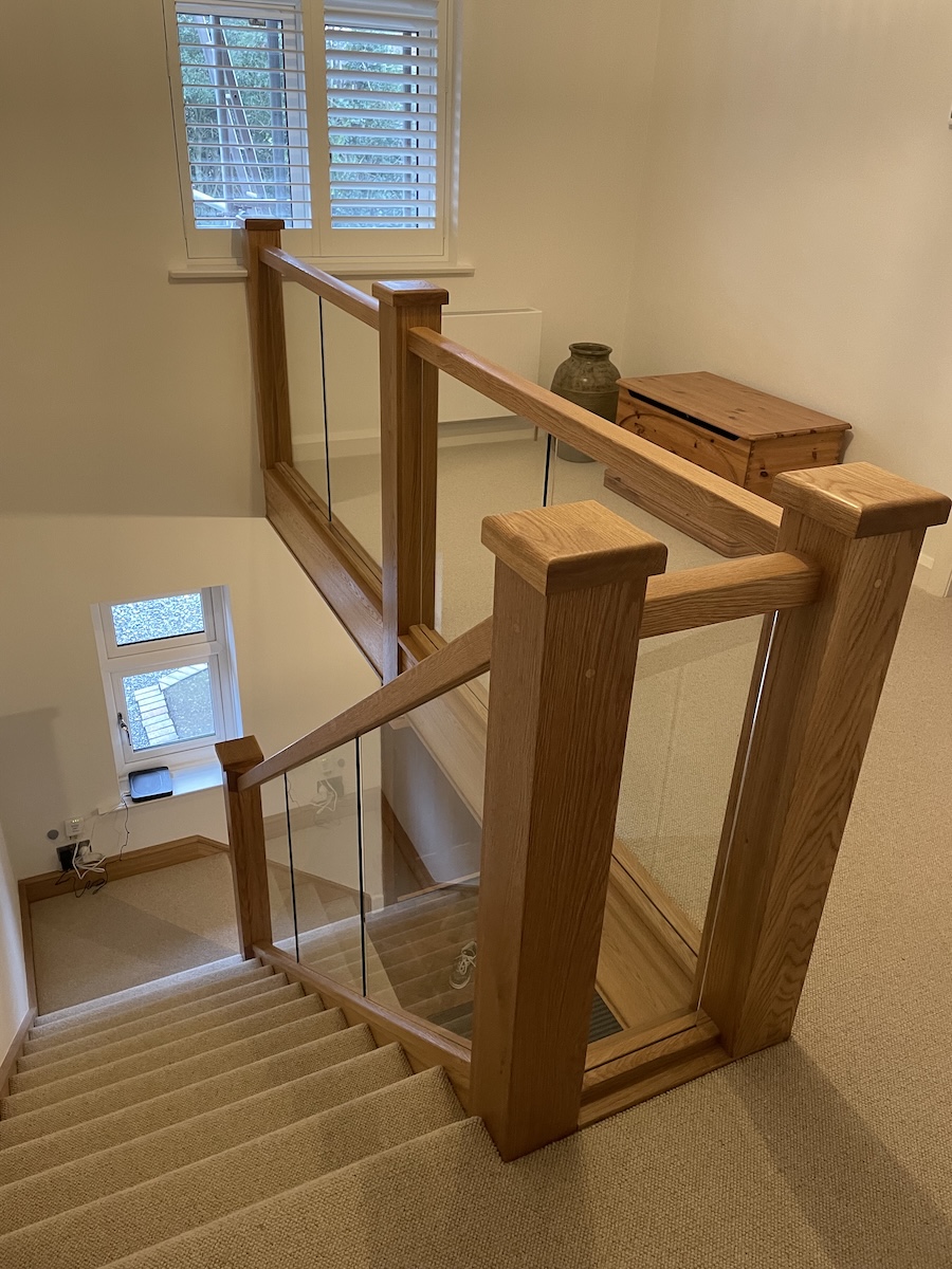 Staircase renovation in Broughton Astley featuring American white oak components with a clear oil finish and glass balustrade panels mounted on chrome brackets. A bright, modern hallway transformation completed in two days by Robert McVey Staircases.