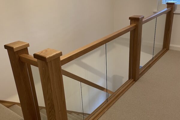 Staircase renovation in Broughton Astley featuring American white oak components with a clear oil finish and glass balustrade panels mounted on chrome brackets. A bright, modern hallway transformation completed in two days by Robert McVey Staircases.