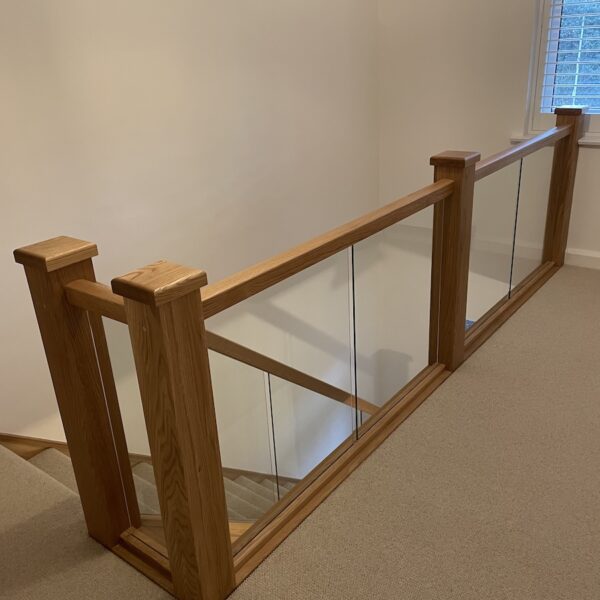 Staircase renovation in Broughton Astley featuring American white oak components with a clear oil finish and glass balustrade panels mounted on chrome brackets. A bright, modern hallway transformation completed in two days by Robert McVey Staircases.