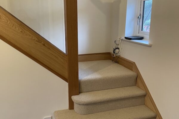 Staircase renovation in Broughton Astley featuring American white oak components with a clear oil finish and glass balustrade panels mounted on chrome brackets. A bright, modern hallway transformation completed in two days by Robert McVey Staircases.