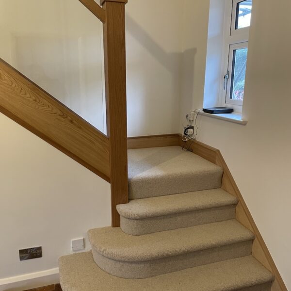 Staircase renovation in Broughton Astley featuring American white oak components with a clear oil finish and glass balustrade panels mounted on chrome brackets. A bright, modern hallway transformation completed in two days by Robert McVey Staircases.